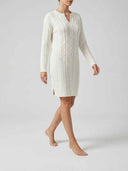 Cream cable-knit mini dress with long sleeves, split notch neckline, and ribbed hem band — angled side view.
