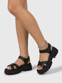 Black chunky platform sandals with lug sole worn on feet, angled view showing crossover straps and ankle strap detail.