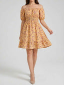 Daisy floral off-shoulder mini dress with smocked bodice, short puff sleeves and A-line ruffle skirt in warm yellow ditsy floral, front view on white background.