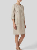 Daisy 3/4 sleeve relaxed shift dress in oat crisp-touch woven, three-quarter roll-tab sleeves and partial button placket, side view on model.