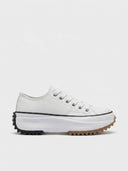 White platform trainers with chunky white midsole and black and brown jagged ripple outsole, side view on white background.