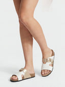 Double-strap leather flat sandals in white and gold worn on feet, angled view showing cork footbed and buckle detail.