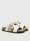 White and gold adjustable leather slide sandals with cork sole, angled product shot on white background.