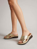 Gold cross-strap espadrille wedge mule sandals on feet, showing cushioned tan footbed and dark lug sole, angled view.