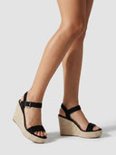 Black suede-look espadrille wedge sandal with woven jute rope sole and silver buckle ankle strap, angled side view.