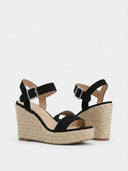Close-up of black suede-look espadrille wedge sandal upper and buckle ankle strap detail, angled view.