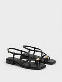 Black strappy flat sandals with gold orb accent at toe strap junction, angled view on white background.