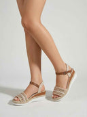 Pair of beige espadrille wedge sandals with beaded embroidered strap, tan ankle straps and white rubber soles, angled three-quarter view.
