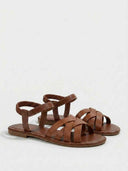 Flat brown sandals with smooth crisscross straps and elastic ankle strap, product shot on white background.
