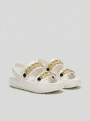 Chunky white platform sandals with gold chain links and polished black bead charms across moulded forefoot straps, angled view on light background.
