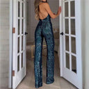 Teal sequin jumpsuit with open back, angled view from behind, standing in a doorway.