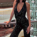 Black sparkly jumpsuit with deep V-neck and cutout detail, angled view indoors by a railing.