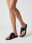 Black cross-strap flat slide sandals with gold buckle detail, worn on feet, angled view on white background.