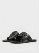 Black flat slide sandals with wide cross-strap and gold buckle accent, angled three-quarter view on white background.