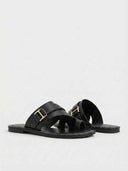 Black wide fit flat slide sandals with gold buckle hardware, angled view showing cushioned footbed and rubber outsole.