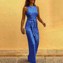 Blue sequin jumpsuit with tie waist, angled front view on yellow wall background.