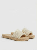 Flat espadrille slide sandals in cream with fringe-trimmed woven strap and jute rope outsole, angled product view on white background.
