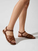 Brown flat strappy sandals with crisscross straps and elasticated ankle strap worn on feet, angled view showing fit.