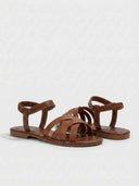 Brown flat open-toe sandals with multi-strap vamp and elasticated ankle strap, three-quarter view showing sole profile.