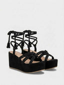 Pair of black rope platform wedge sandals with ankle-wrap lace-up fastening, angled view on white background.
