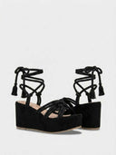 Pair of black braided rope platform wedge sandals with tassel tie ankle wrap, angled view on white background.