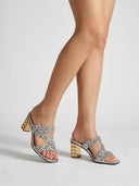 Silver sequin block heel mules with gold pyramid-studded block heel, worn on feet, angled three-quarter view.