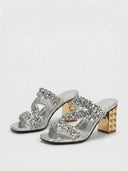Silver sequin-embellished heeled mules with gold studded block heel, angled view on white background.