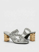 Silver sequin crossover strap mules with gold pyramid-studded block heel, close angled view showing heel detail.