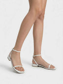 White square-toe strappy sandals worn on a model, showing adjustable ankle strap and low block heel, angled view on white background.
