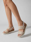 Feet wearing beige espadrille wedge sandals with embroidered geometric wide strap and silver slingback ankle strap, angled view.