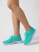 Teal mesh lace-up trainers with white cushioned soles worn on feet, angled side view.