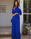 Blue jumpsuit with cold shoulder detail, wrap top, and tie waist, front view.