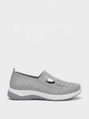 Grey slip-on knit trainers with T-bar cutout strap detail and cushioned white midsole — front view on white background.
