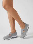 Grey slip-on knit trainers with perforated mesh upper and contoured cushioned sole — angled view showing T-bar strap and heel pull tab.