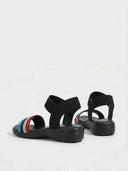 Pair of striped elastic flat sandals showing ridged rubber outsole and ankle band, rear angled view on white background.