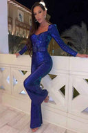 Woman in blue sequin jumpsuit with belted waist, posing on a balcony at night, full view.