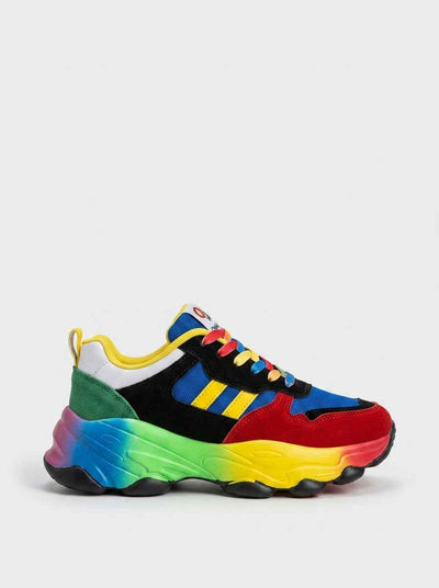 Chunky lace-up trainers with rainbow bubble sole and multicolour upper — blue, red, black and green panels, side profile on white background.