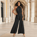 Black pleated halter jumpsuit with tie waist, front view on an arched walkway.