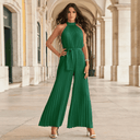Green pleated halter jumpsuit with tie waist, front view on an outdoor arched walkway.