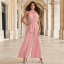 Pink pleated halter neck jumpsuit with tie waist, front view in an arched hallway.