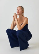Navy spaghetti strap overall with flared hem, model crouching, front angled view.
