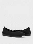 Close-up of ribbed knit upper and heel pull-tab on black women's ballet flat with cushioned insole.