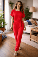 Red wide-leg jumpsuit with short sleeves and a tied waist belt, front view on a wooden floor.