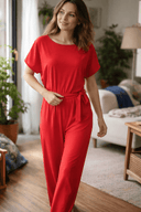 Red wide-leg belted jumpsuit with short sleeves, front view in a living room.