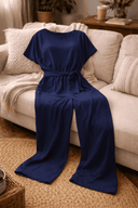 Navy wide-leg belted jumpsuit with short sleeves, angled view on a sofa.