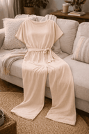 Pale pink wide-leg jumpsuit with short sleeves and tied waist, draped on a sofa, front view.