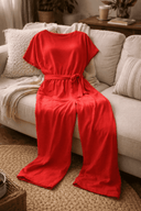 Red wide-leg belted jumpsuit with short sleeves, front view on a light gray sofa.
