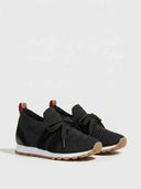 Black knit lace-up trainer showing white midsole and gum rubber outsole tread, angled side view.