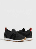 Black knit barefoot trainer with flat bow laces, white sole, and red heel pull tab, angled rear-side view.