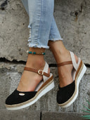 Black closed-toe espadrille wedge sandals with tan buckle ankle strap and jute sole trim, worn with cropped jeans, angled view.